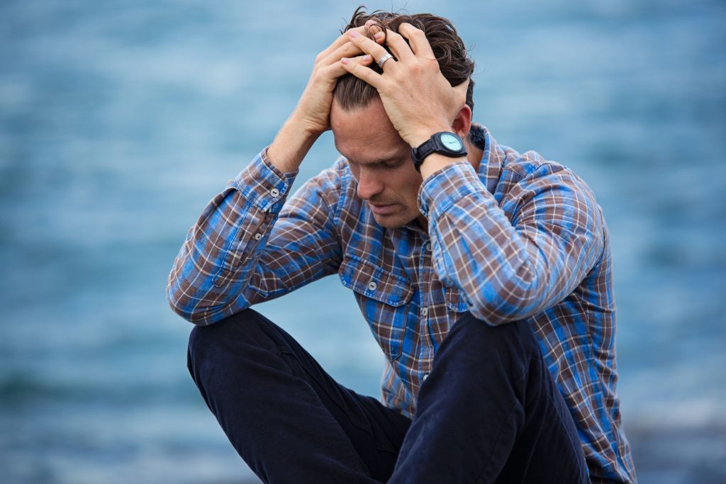 Stressed man sitting in front of water, running his hands through his hair.