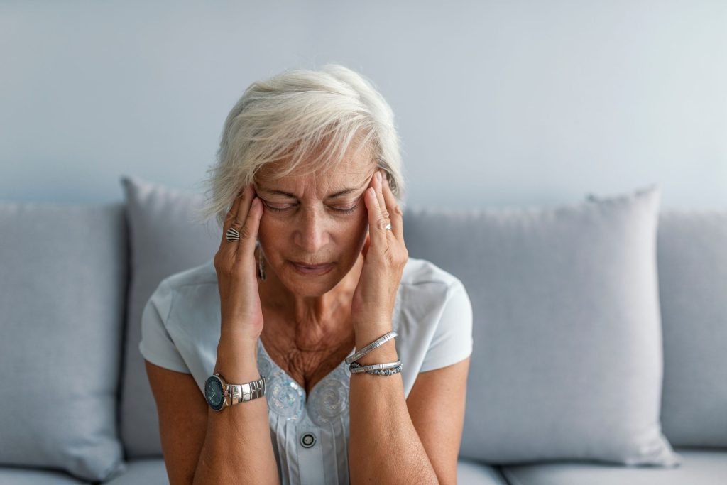 Woman sitting on her couch with hands on temples with a headache